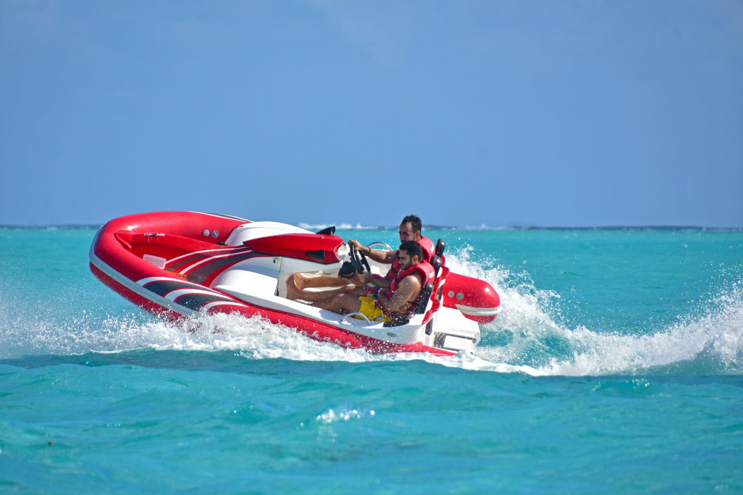 Two men speed through turquoise waters on a red and white SeaKart inflatable motorized watercraft.